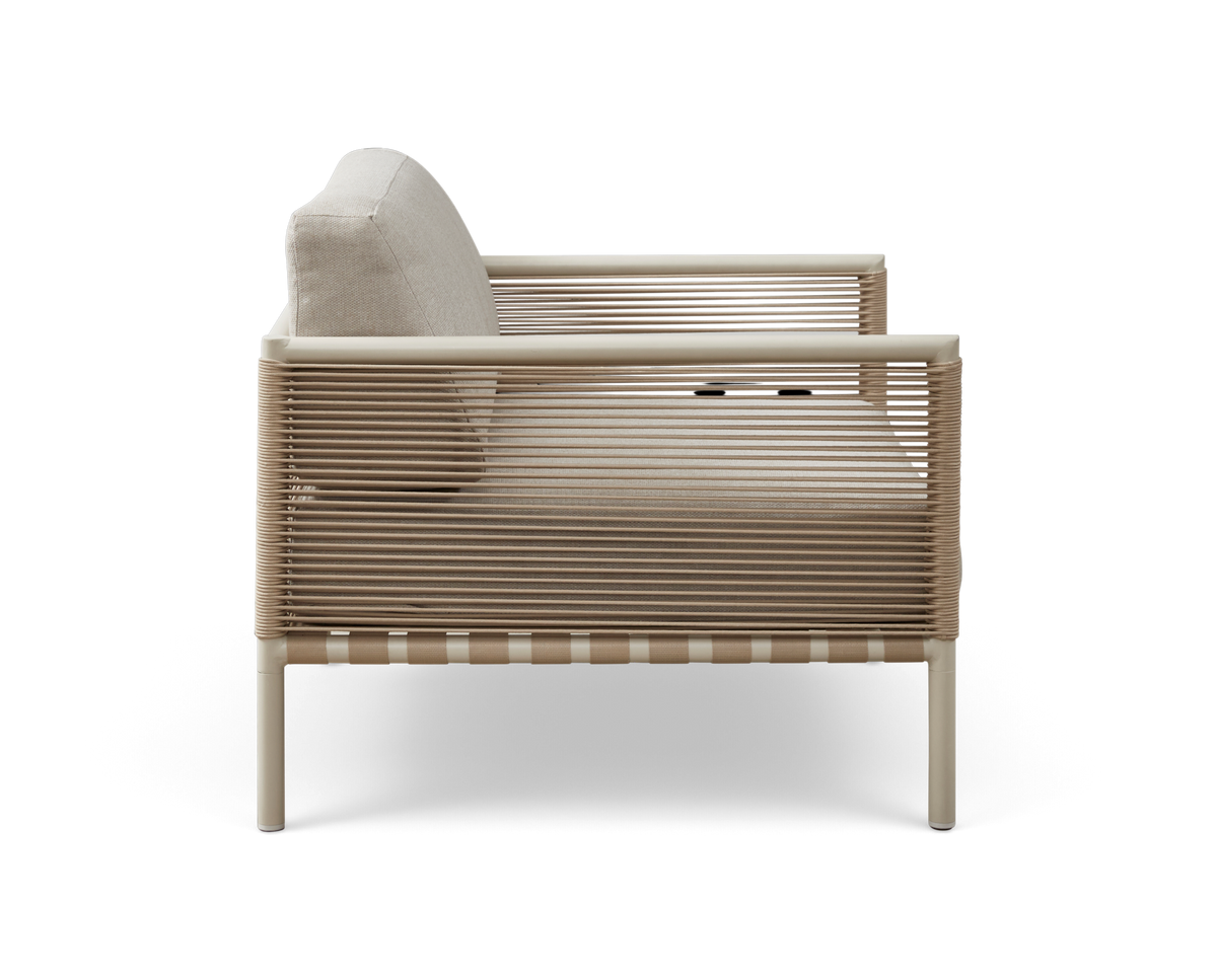 Beige loungestol med snoromviklede sider, set fra siden med lyse hynder, frilagt på hvid baggrund.