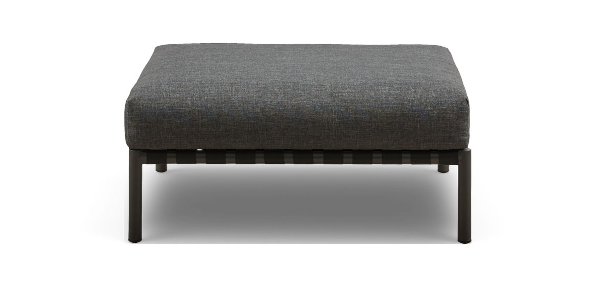Grå polstret ottoman/fodskammel med metalben, set forfra mod sort baggrund.