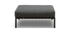 Grå polstret ottoman/fodskammel med metalben, set forfra mod sort baggrund.