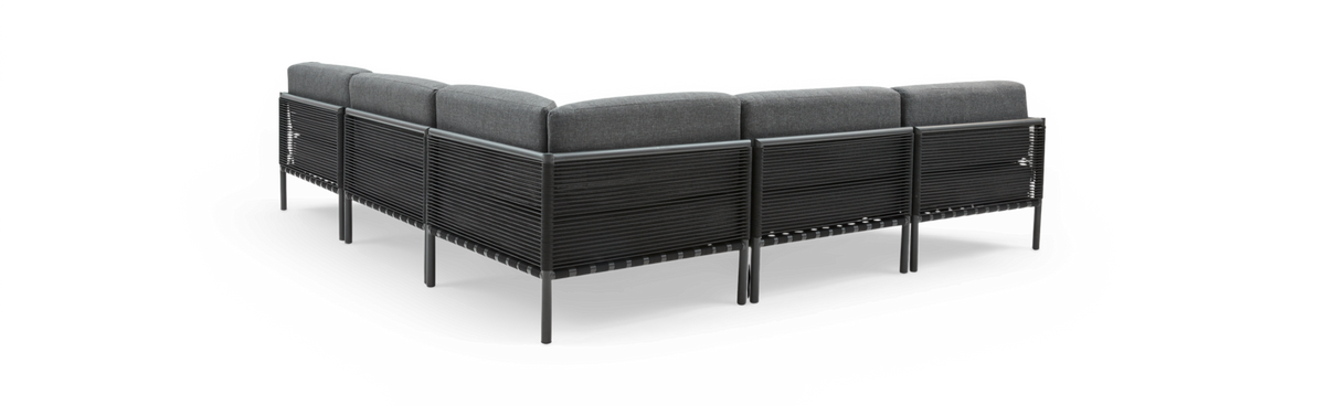 Modulær L‑sofa til udendørs brug med mørkegrå puder og sort snorre-ramme, set skråt bagfra på hvid baggrund.