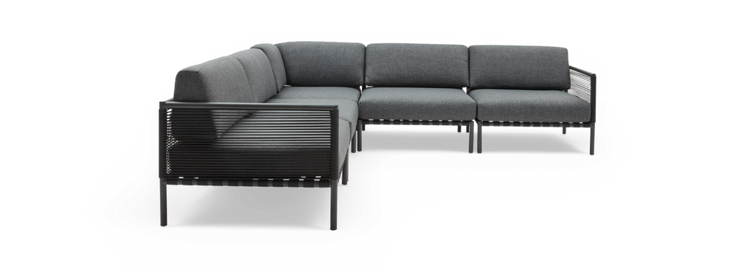 Modulær hjørnesofa i mørkegråt stof med sort ramme, frilagt på sort baggrund.
