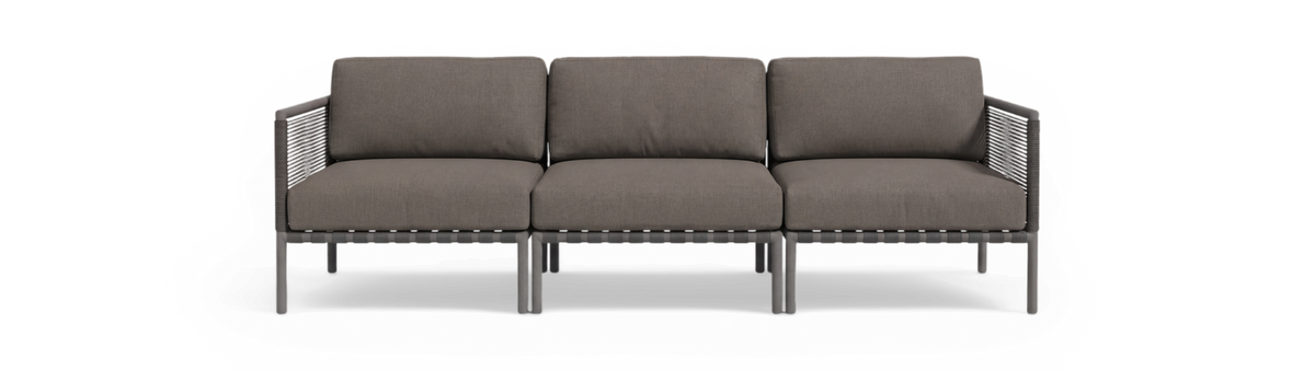 Modulær 3-personers sofa i gråt stof med hynder og flettede armlæn, frilagt på sort baggrund.