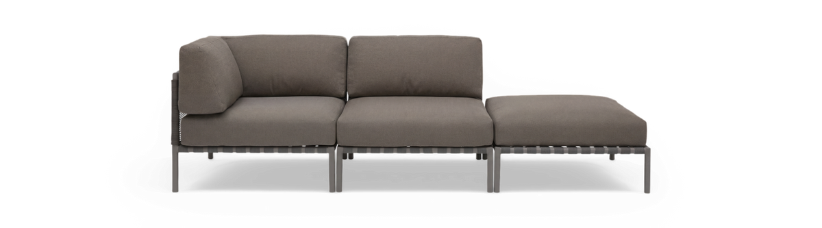Modulær 3-personers sofa med chaiselong i grå, frontvisning mod sort baggrund.