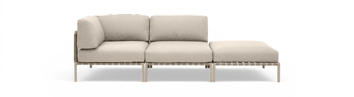 Beige modulsofa med venstre hjørnemodul, midtersektion og chaiselong/ottoman på række, set forfra på frilagt baggrund.