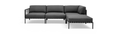 Mørkegrå modulsofa i L‑form med chaiselong til højre, fritstående mod sort baggrund.
