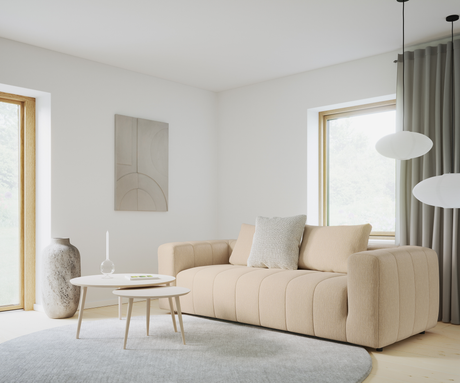 Lys skandinavisk stue med beige sofa, to runde hvide sofaborde med lys og glasdekoration, stort gråt rundt tæppe, stenvase, abstrakt vægkunst og rispapirspendler ved vinduer med grå gardiner.