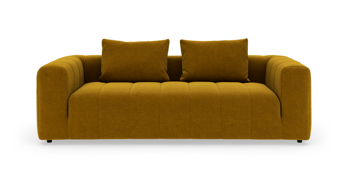 Sennepsgul stofsofa med to matchende puder, set forfra mod hvid studiobaggrund.
