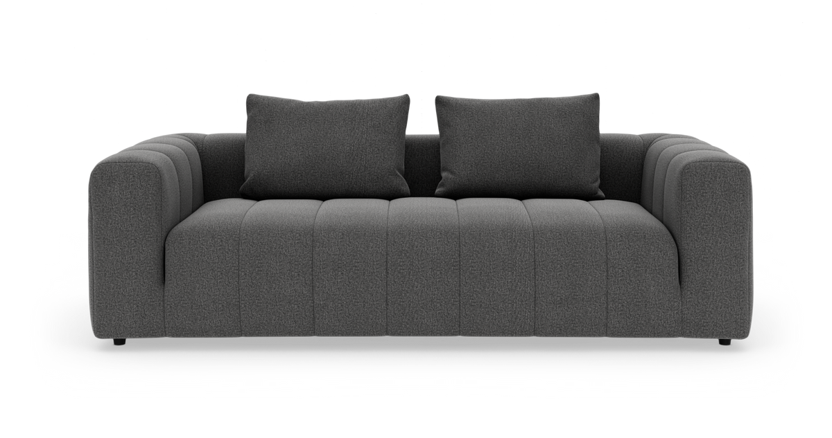 Mørkegrå 3-personers sofa med to puder, afrundede armlæn og lodrette panel-syninger, frilagt på hvid baggrund.