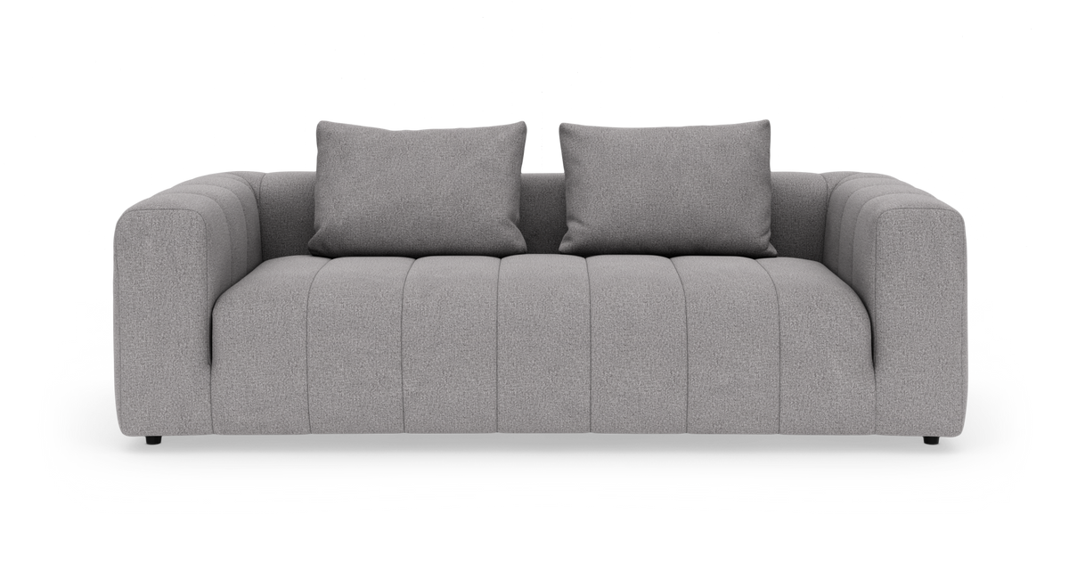 Grå tresæders sofa med brede armlæn og to puder, fritlagt på hvid baggrund.