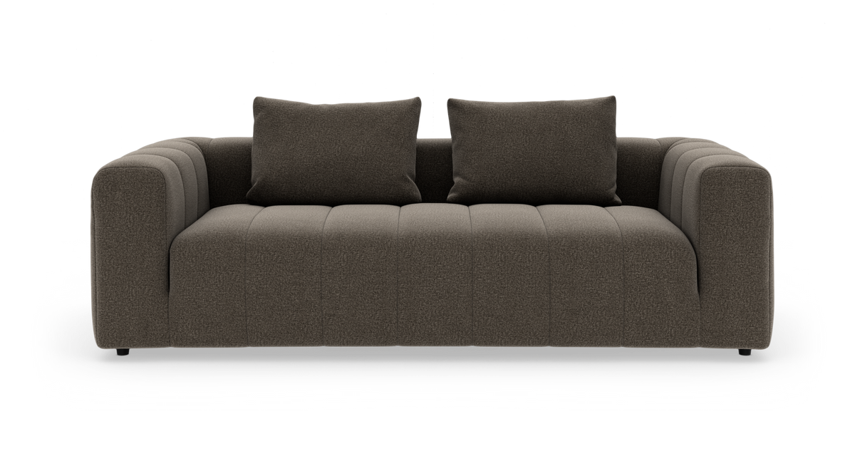Brun stofsofa med to løse rygpuder og brede, afrundede armlæn, frilagt mod hvid baggrund set forfra.
