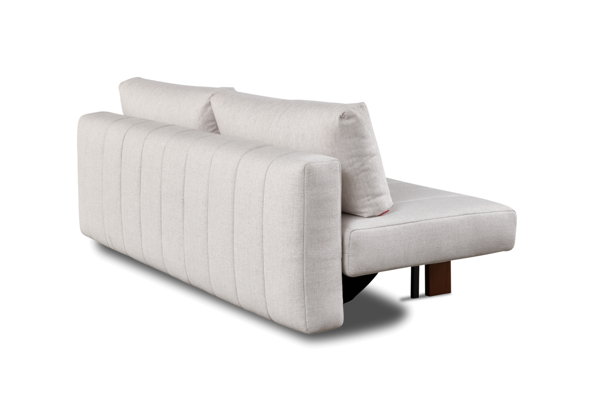 Lys beige modulsofa med kanalstik på ryggen og to løse ryghynder, fotograferet skråt bagfra på sort baggrund.