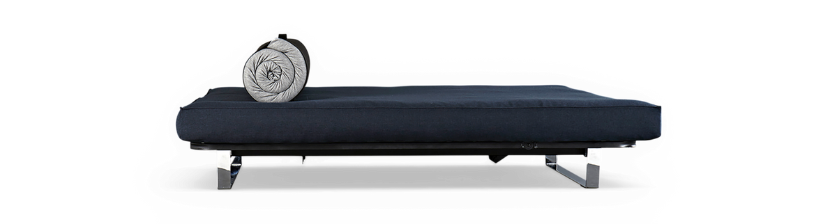 Mørkeblå daybed med kromben og rullet grå bolsterpude på sort baggrund.