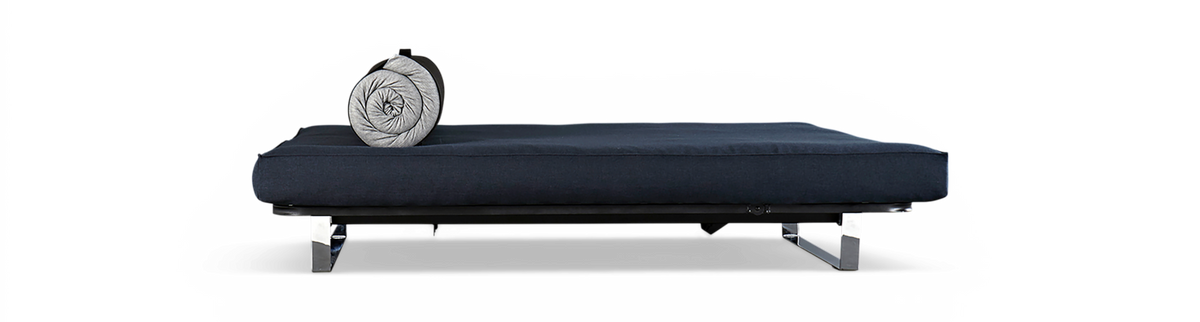 Mørkeblå daybed med kromben og rullet grå pude på sort baggrund.