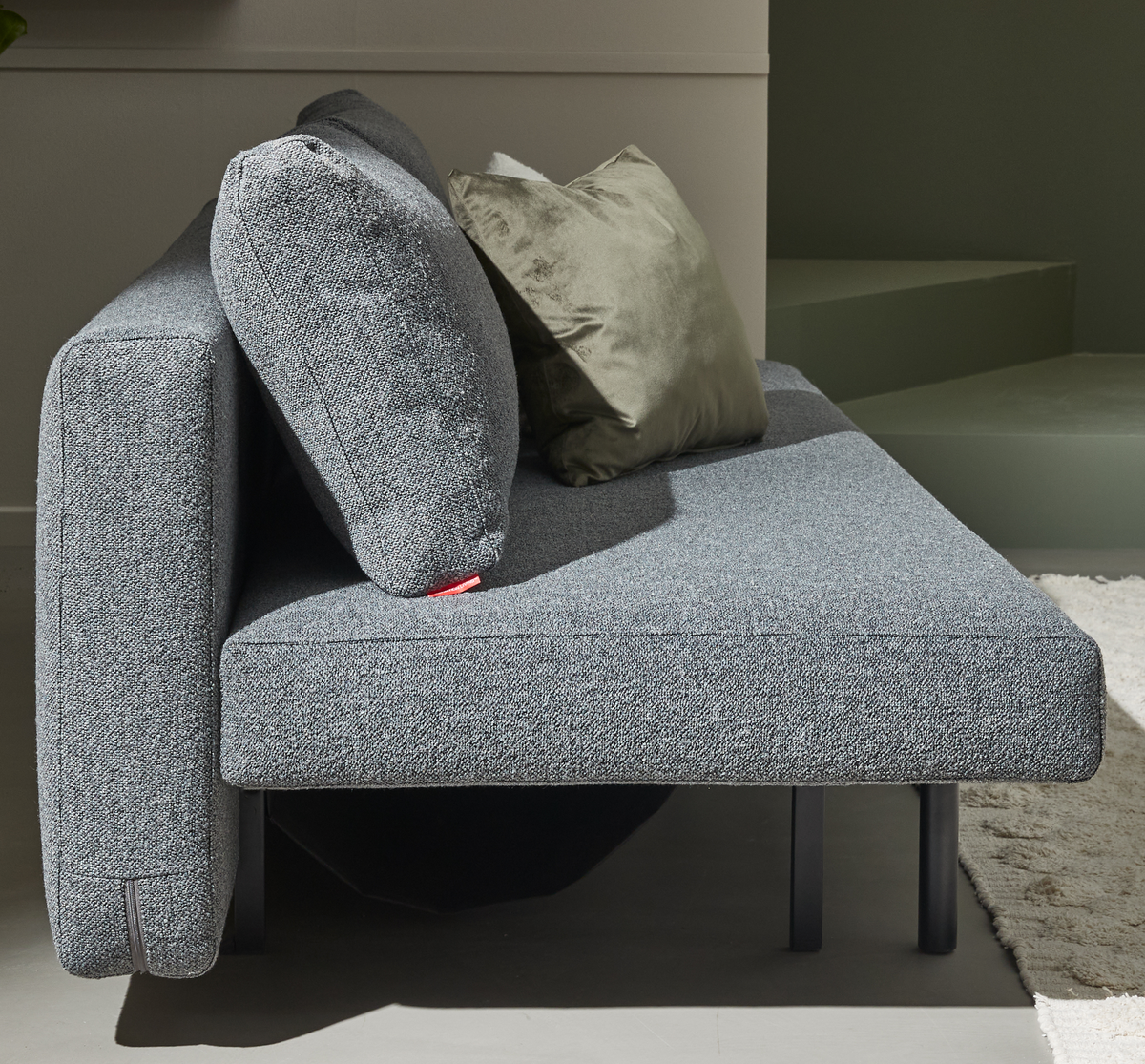 Grå moderne sofa set tæt på fra siden med to puder, heraf en grøn velourpude, i en lys stue.