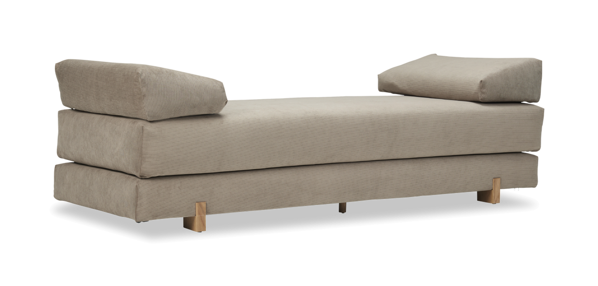 Beige daybed i cordfløjl med to skrå puder og træben, frilagt.