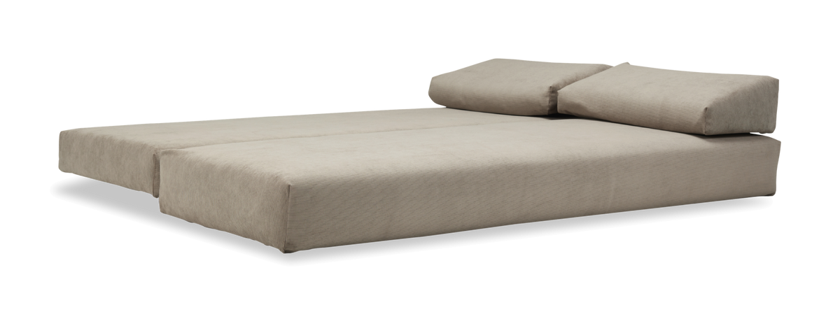 Beige modulsofa/seng i udfoldet, fladt leje med to ryghynder på frilagt baggrund.