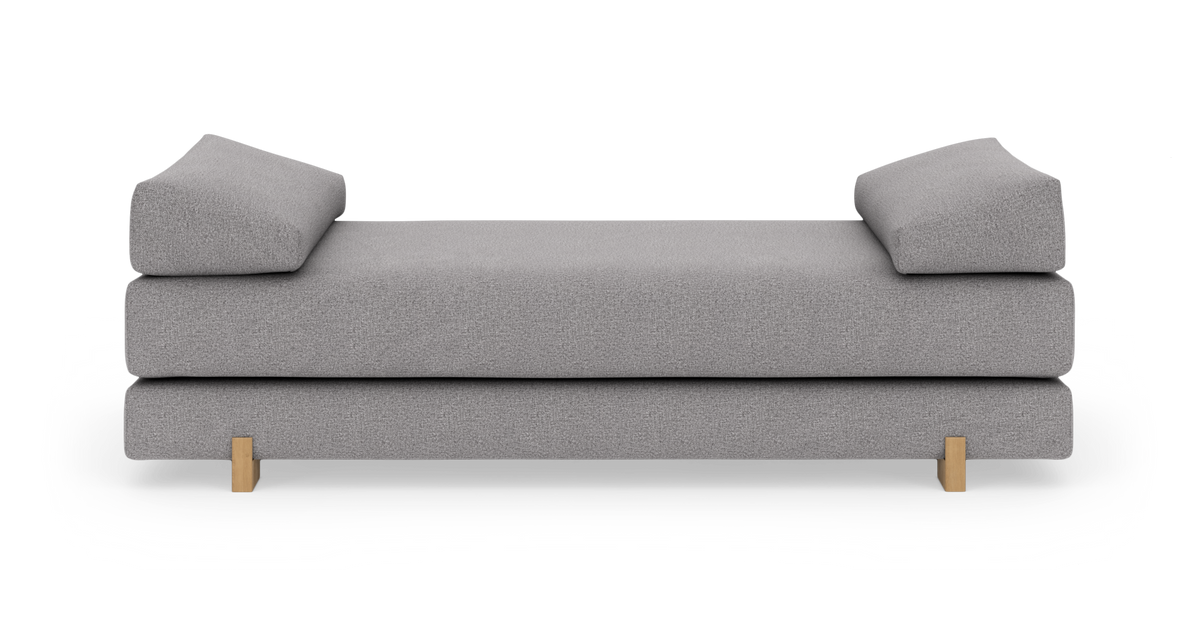 Grå daybed/sofa med to skrå armpuder og træben, fritlagt på hvid baggrund.