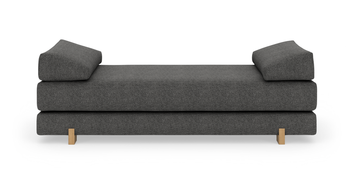 Mørkegrå daybed/sofa med vinklede puder og lyse træben, fotograferet lige for i studiebaggrund.