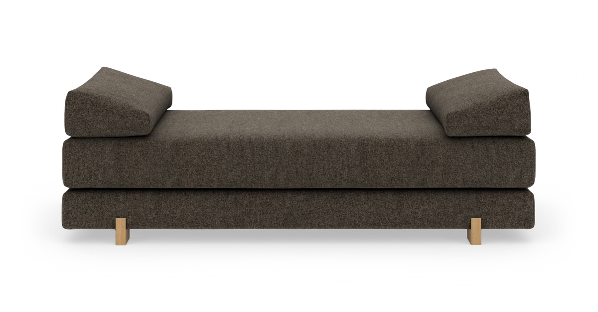 Mørkebrun daybed/sofa med vinklede puder og lyse træben, frilagt frontvisning.