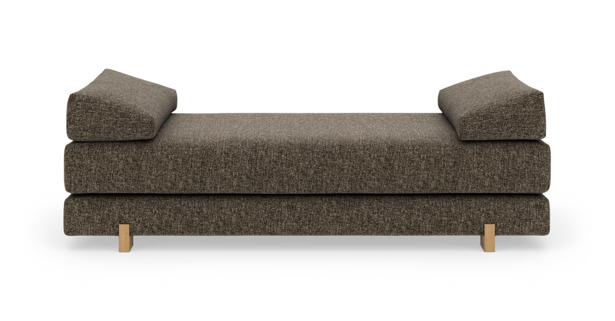 Brun stofbetrukket daybed/sofa med to kileformede armpuder og lyse træben, frilagt på hvid baggrund, frontvisning.