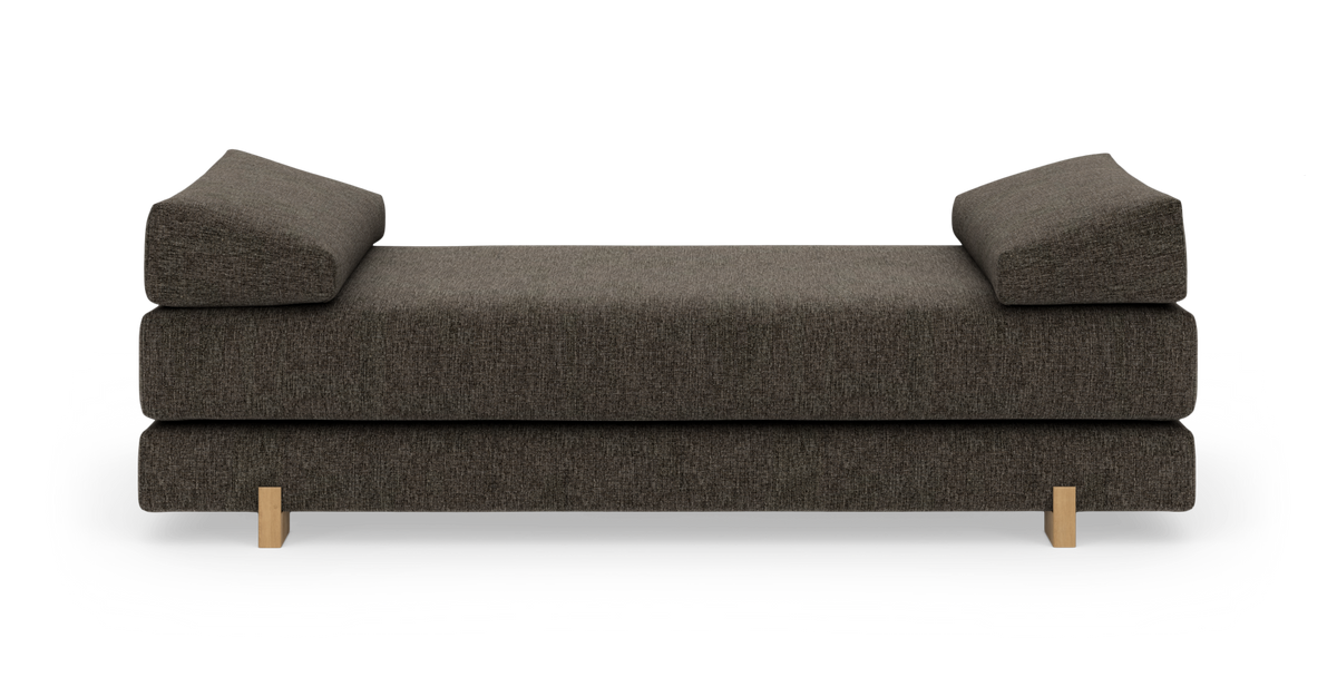 Mørkegrå daybed/sofa med to vinklede armlæn og lyse træben, frilagt på hvid baggrund.
