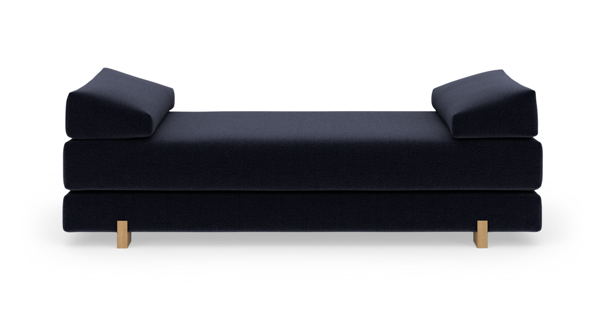 Mørkeblå daybed med to vinklede armlæn og lyse træben, frilagt på hvid baggrund.