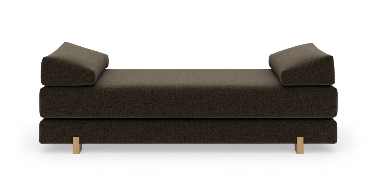Mørkebrun polstret daybed/sofa med to vinklede armlæn og lyse træben, frilagt frontvisning.