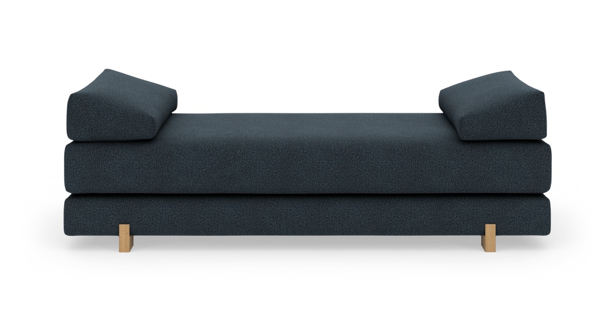 Mørkeblå daybed/sofa med to skrå armlæn og lyse træben, set forfra mod hvid baggrund.