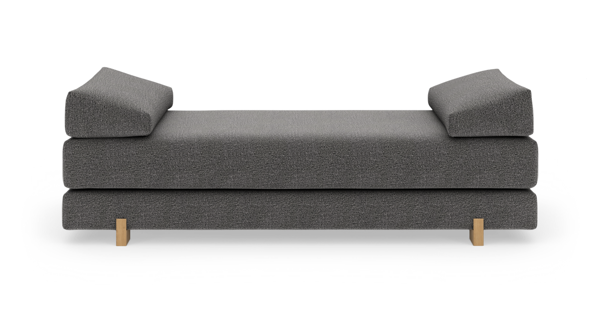 Grå daybed med skrå armlæn og lyse træben set lige forfra.
