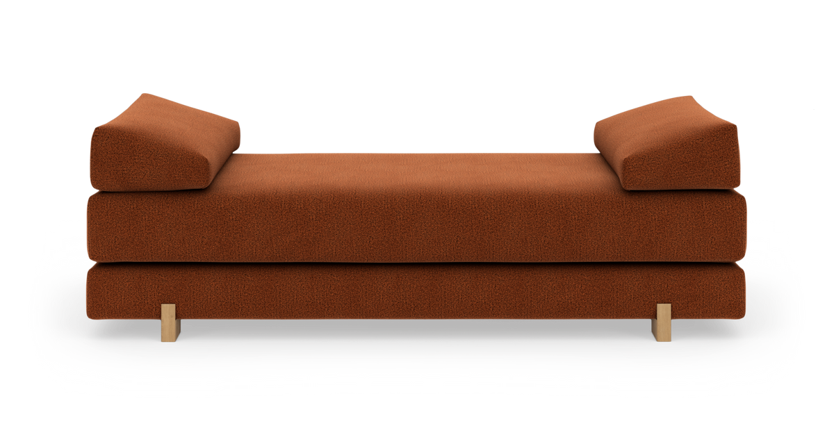 Rustfarvet daybed/sofa med skrå ryghynder og lyse træben på hvid studiebaggrund.