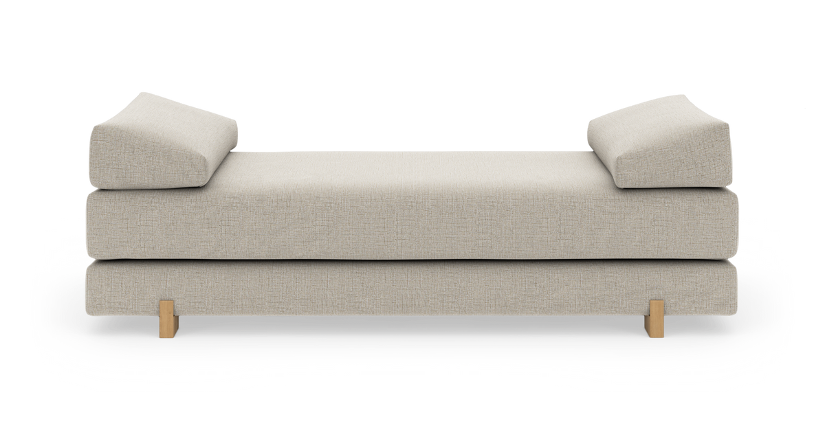 Beige daybed med to skrå pudestøtter og træben, centreret på hvid baggrund.