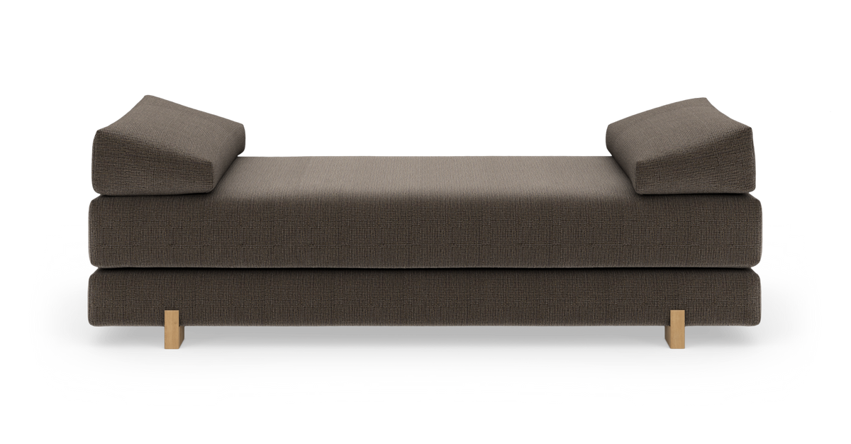Brun daybed med to kileformede armlæn og lyse træben, fritlagt på hvid baggrund, frontvisning.