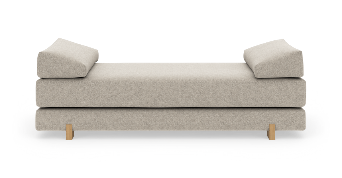 Beige daybed med to vinklede armlænspuder og lyse træben, frilagt på hvid baggrund.