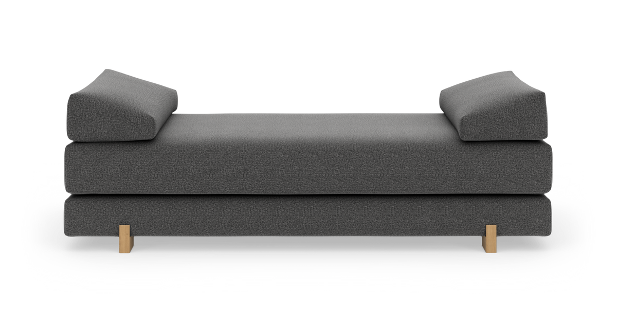 Mørkegrå daybed med skrå armlæn i begge ender og små træben, set lige forfra.