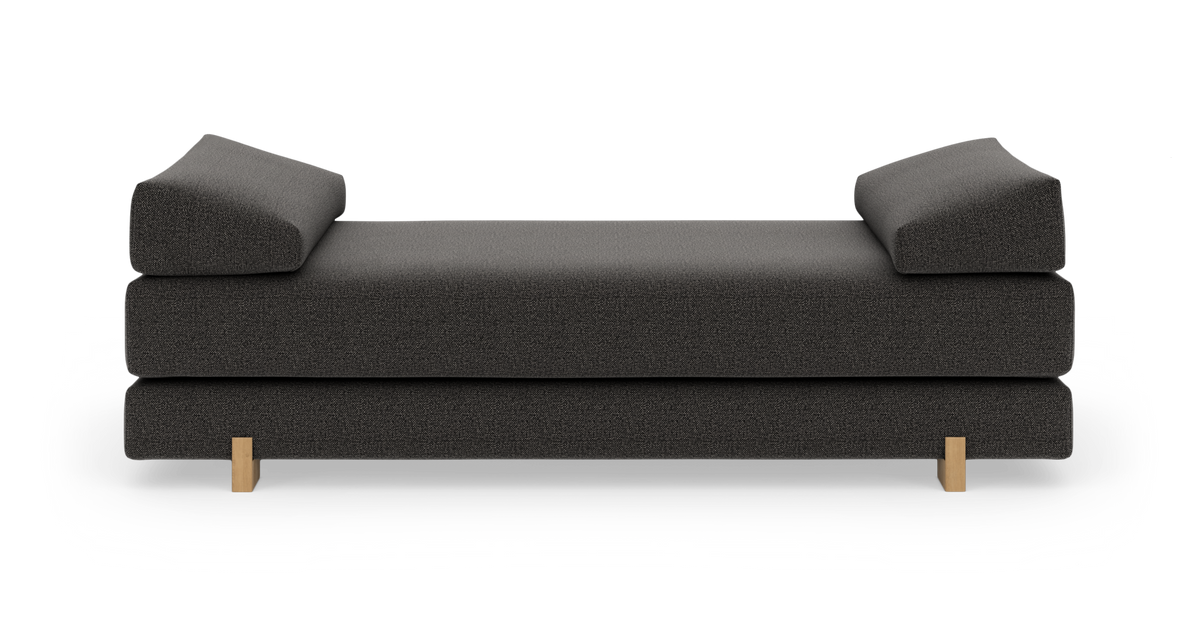 Mørkegrå daybed med to kileformede armlæn og lyse træben, frilagt produktfoto forfra.