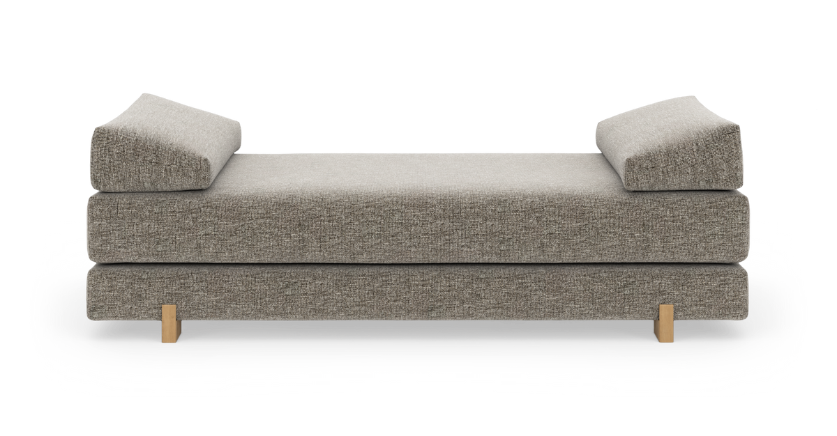 Grå daybed med to kileformede ryglæn/armstøtter og træben, frilagt på hvid baggrund.