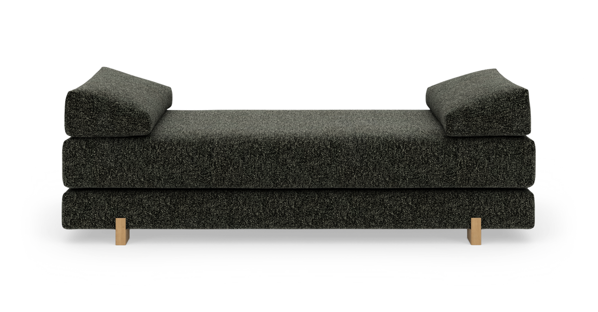 Mørkegrå daybed/sofa med kileformede armlæn og lyse træben, frilagt på hvid baggrund.