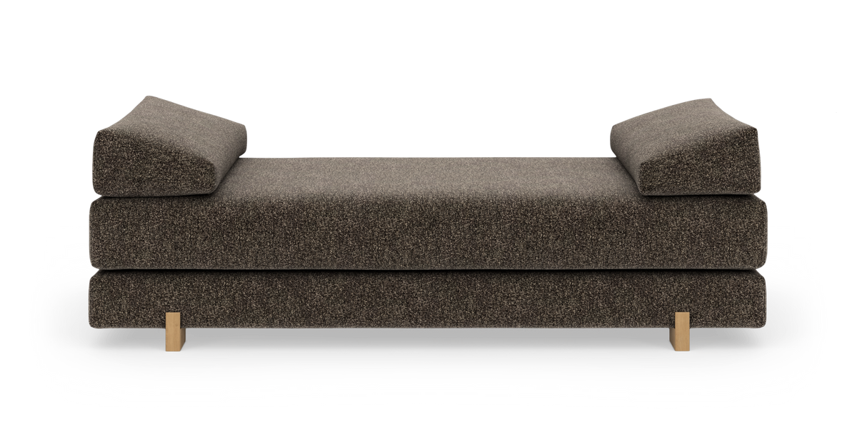 Brun moderne daybed/sofa med skrå armpuder i begge ender og små træben, frilagt på hvid baggrund.
