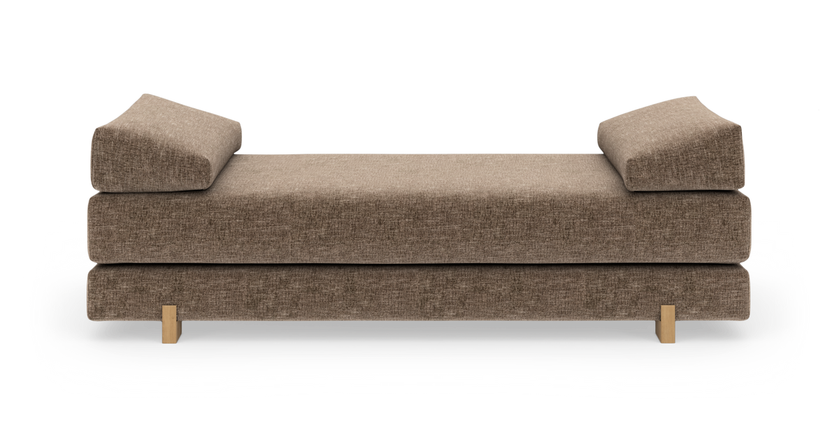 Brun daybed/sofa med to kileformede rygpuder og træben, frilagt på hvid baggrund.