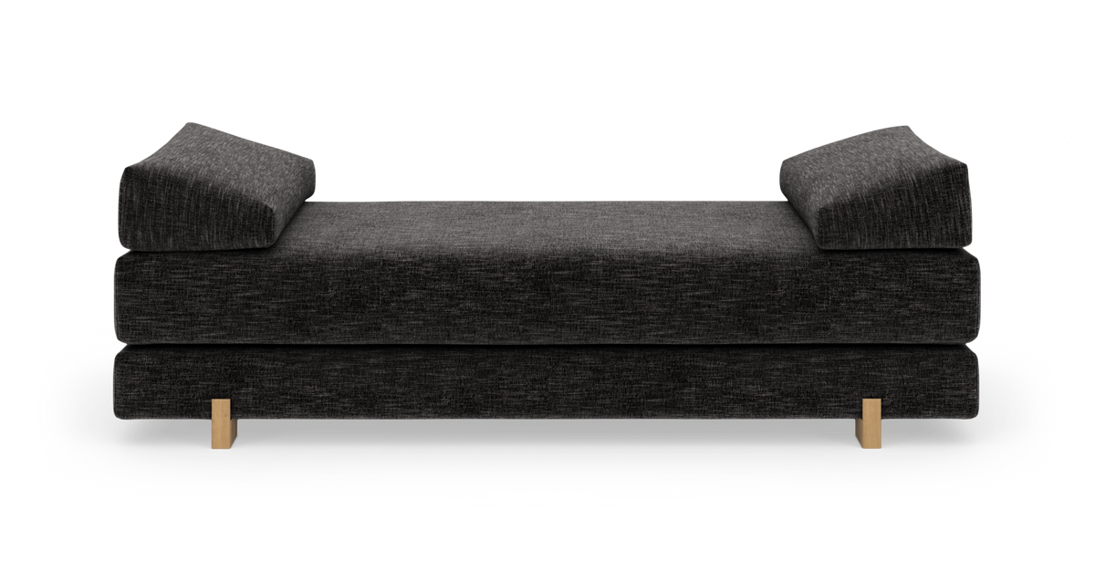 Mørkegrå daybed med to skrå armlæn og lyse træben, fritlagt på hvid baggrund.