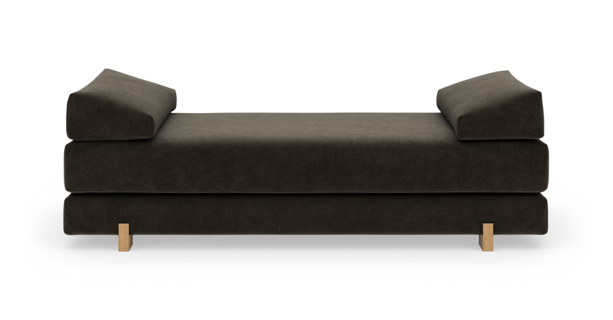 Mørkebrun daybed med vinklede armlæn på begge sider og lave træben, frilagt mod hvid baggrund i frontvisning.