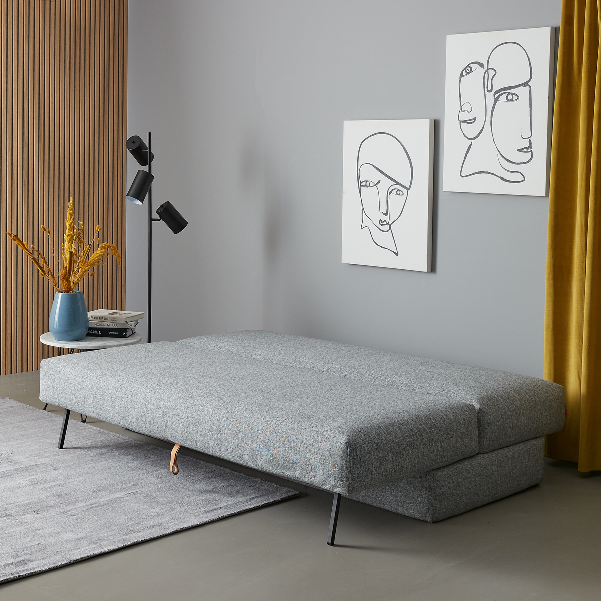 Grå sovesofa udslået i moderne stue med sort gulvlampe, lineart-vægkunst og gul gardin.