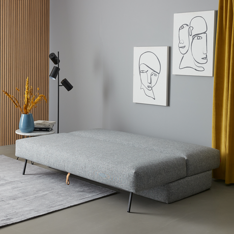Grå sovesofa udslået i moderne stue med sort gulvlampe, lineart-vægkunst og gul gardin.