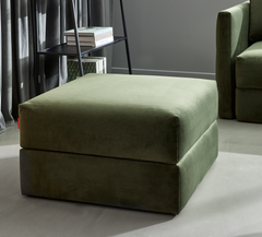 Olivengrøn polstret ottoman i moderne stue ved siden af sofa og reol med bøger i dagslys.