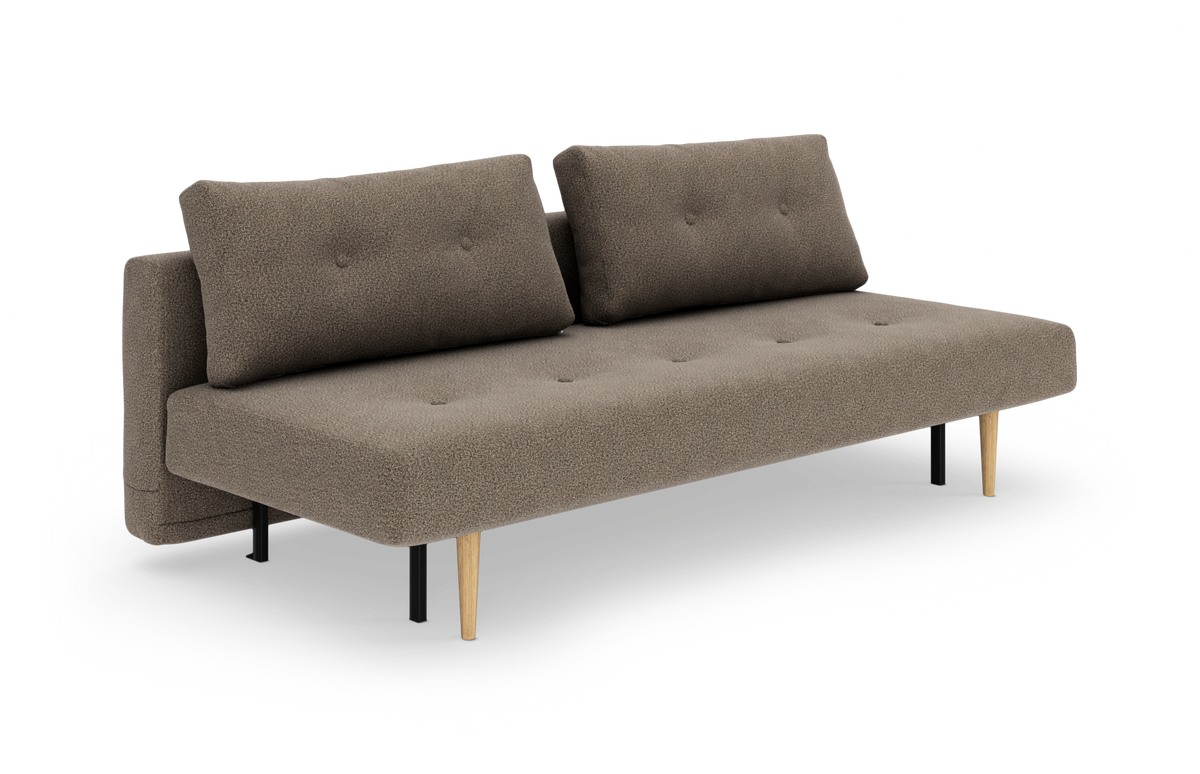 Brun‑beige sovesofa med to rygpuder og koniske ben i sort og eg, frilagt på hvid baggrund.