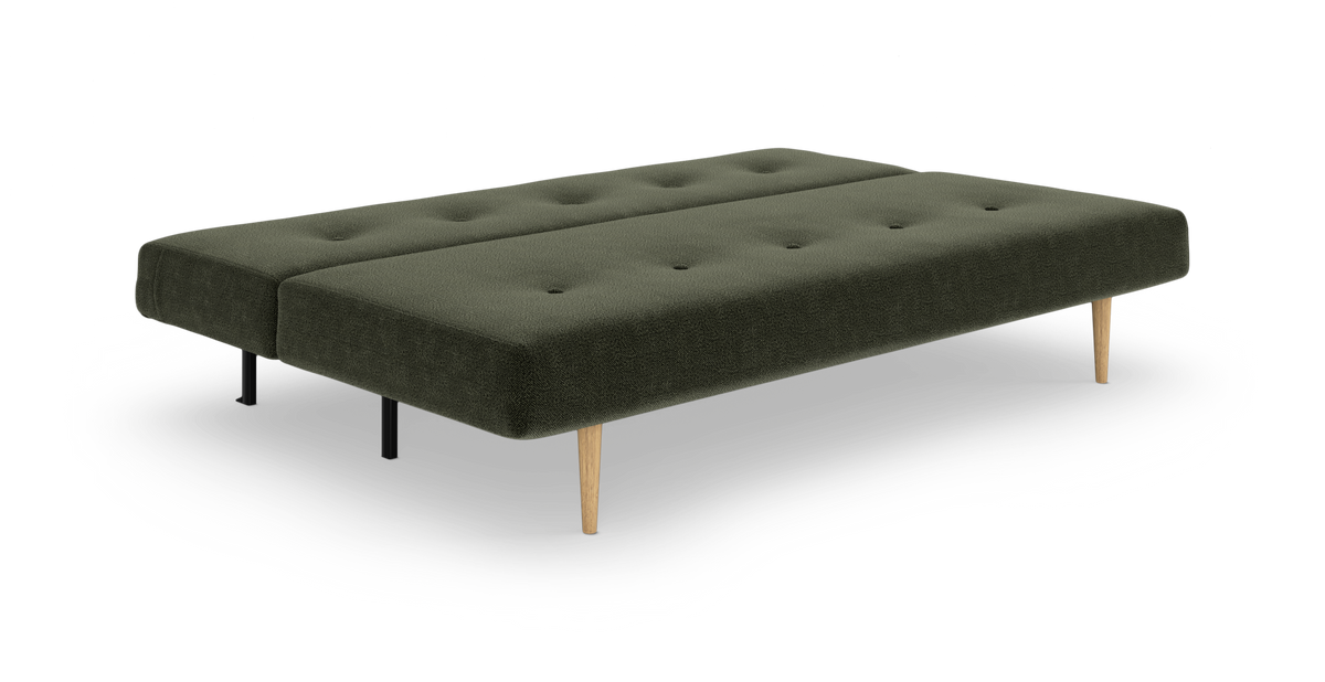 Mørkegrøn sovesofa/daybed i stof med knaptuftet sæde og koniske egetræsben samt sorte støtteben, fritlagt på hvid baggrund.