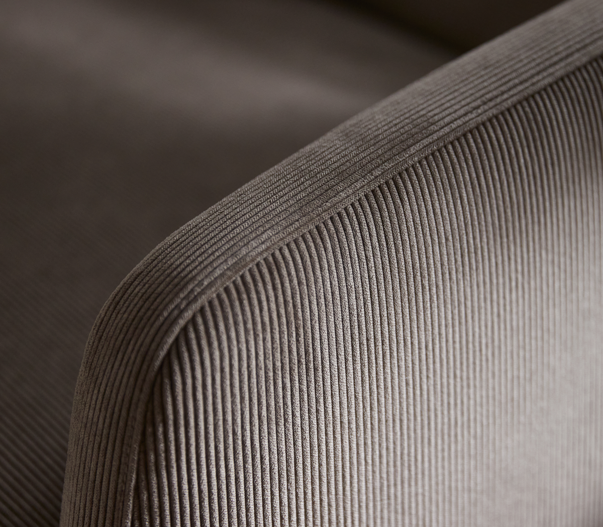Nærbillede af ribbet corduroy/velour-betræk på et beige/taupe sofa-armlæn.