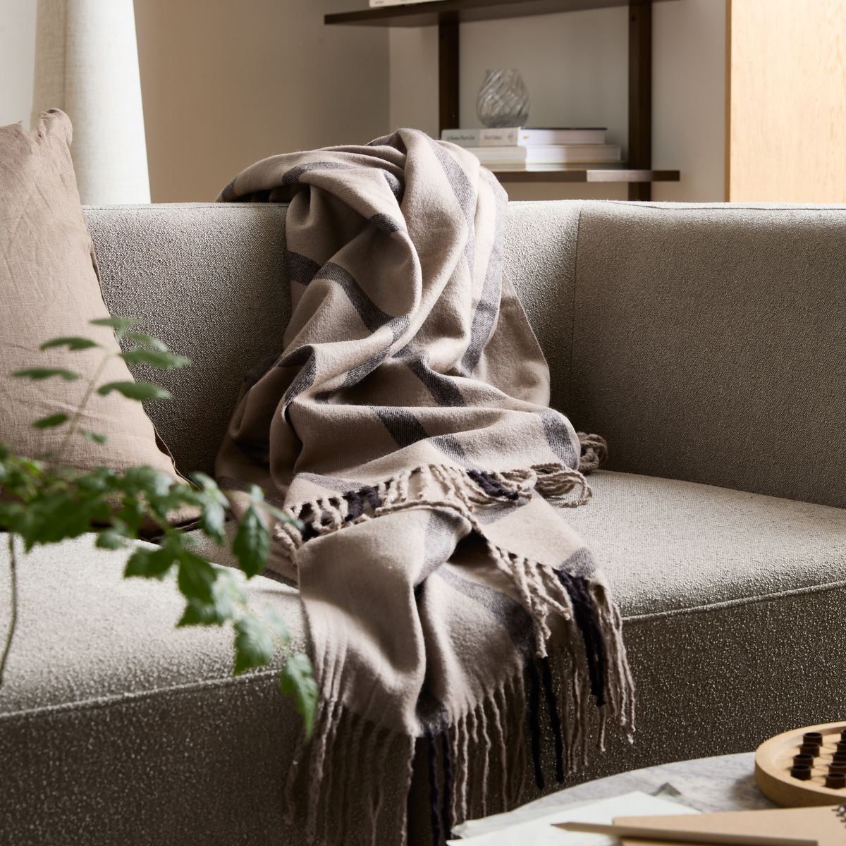 Beige ternet plaid med frynser ligger over en lysegrå sofa i en skandinavisk stue.