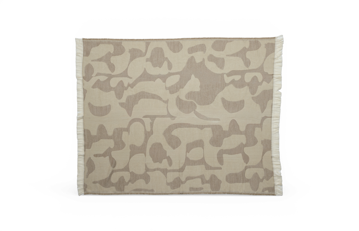 Beige plaid med tone‑i‑tone abstrakt mønster og frynser i kanterne på hvid baggrund.
