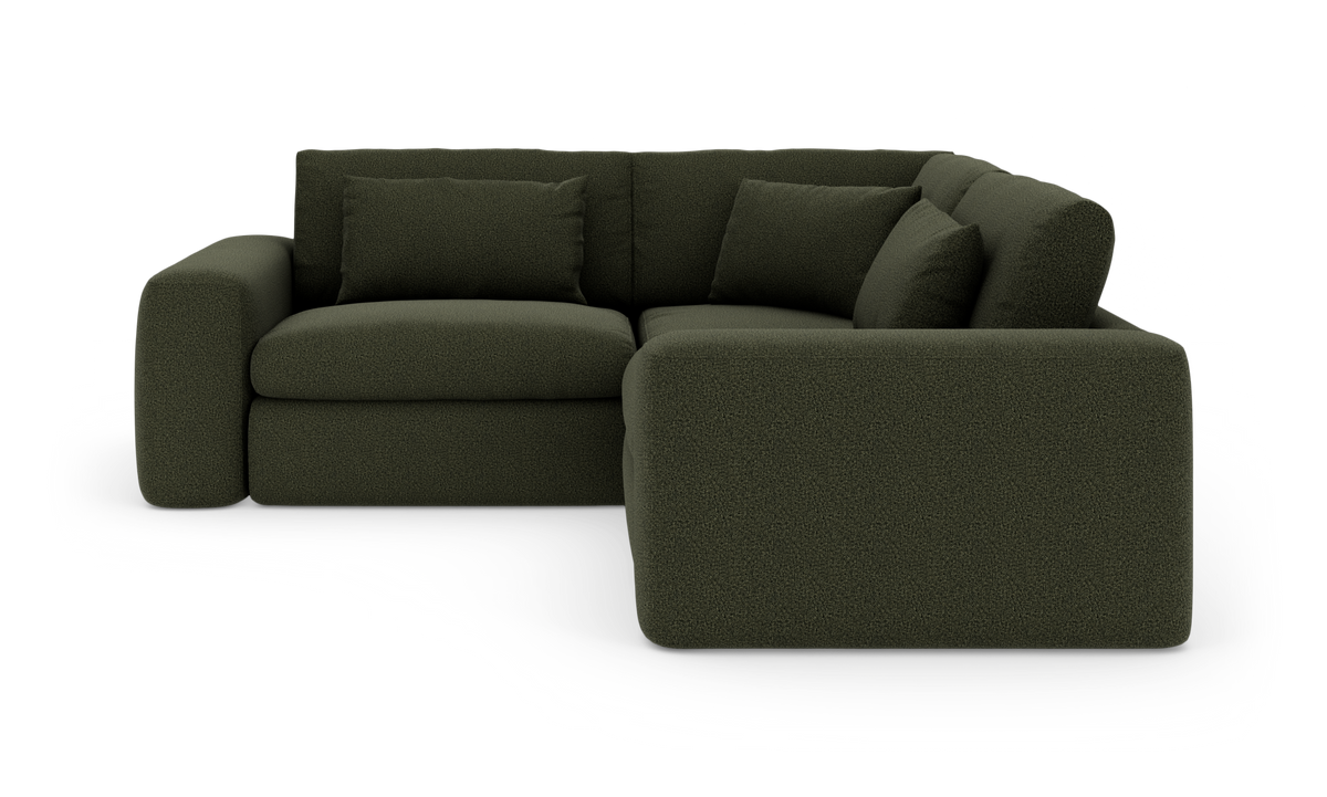 Mørkegrøn L‑sofa med afrundede former og løse puder, frilagt på hvid baggrund.